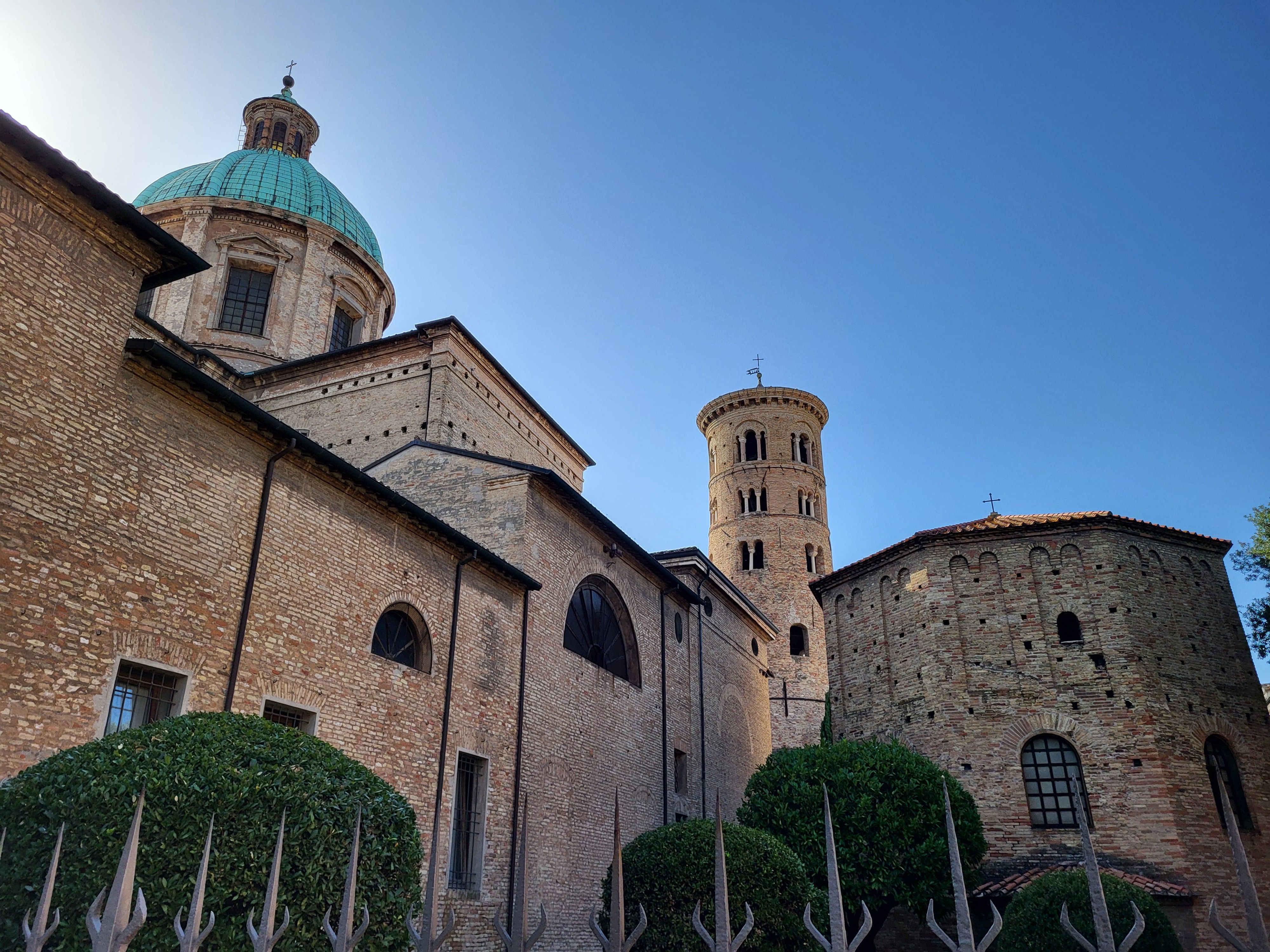 Ancient brick cathedral with a green dome and round tower under a clear blue sky.