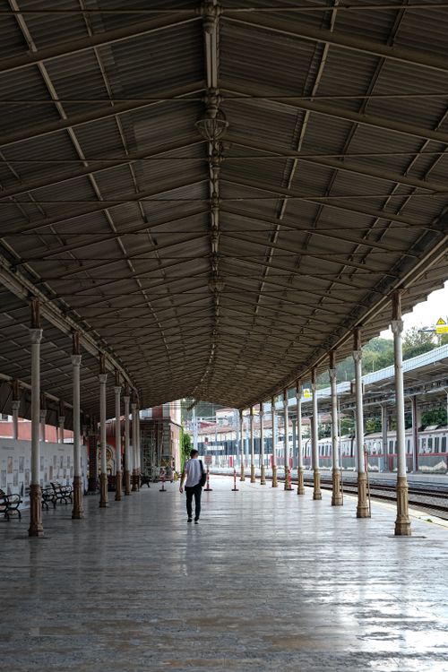 Free A deserted railway station platform with a solitary figure walking under arched steel roofing. Stock Photo