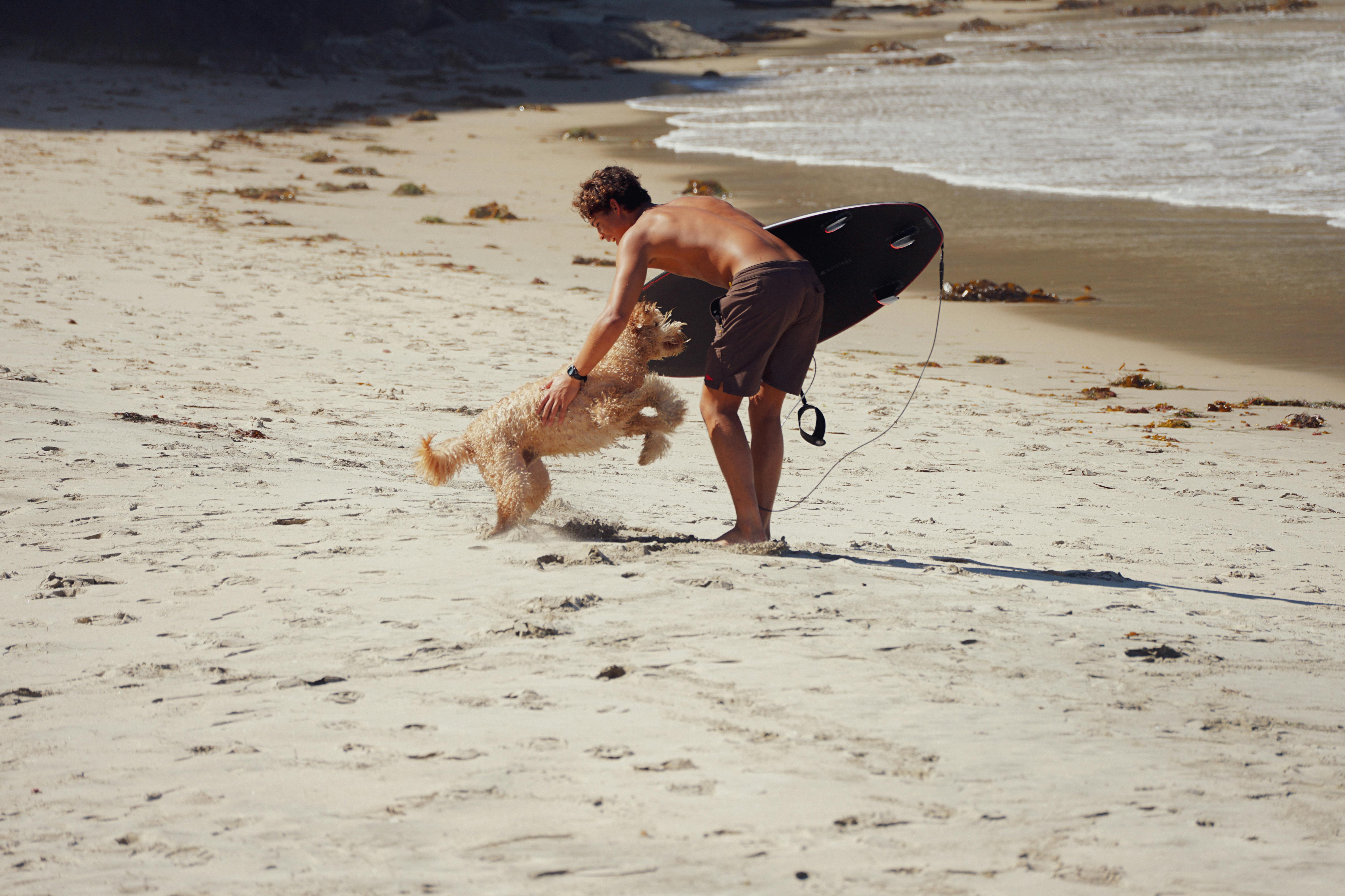 a man holding a surfboard and a dog on the beach