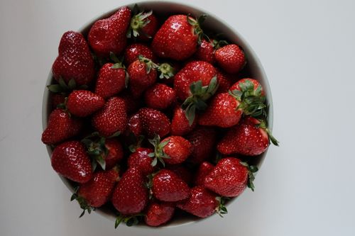 Free Top view of a bowl filled with ripe, juicy strawberries on a white surface. Stock Photo