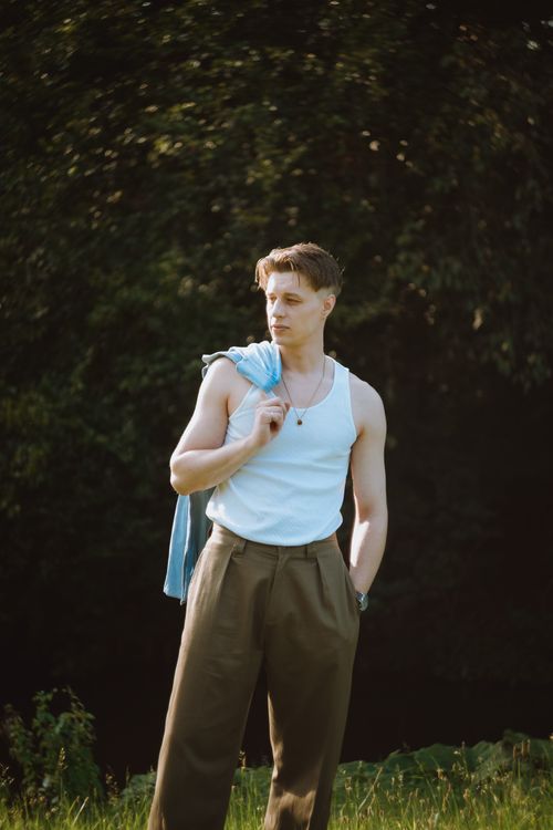 Free Stylish young man in a relaxed pose outdoors, showcasing summer fashion against a lush green backdrop. Stock Photo