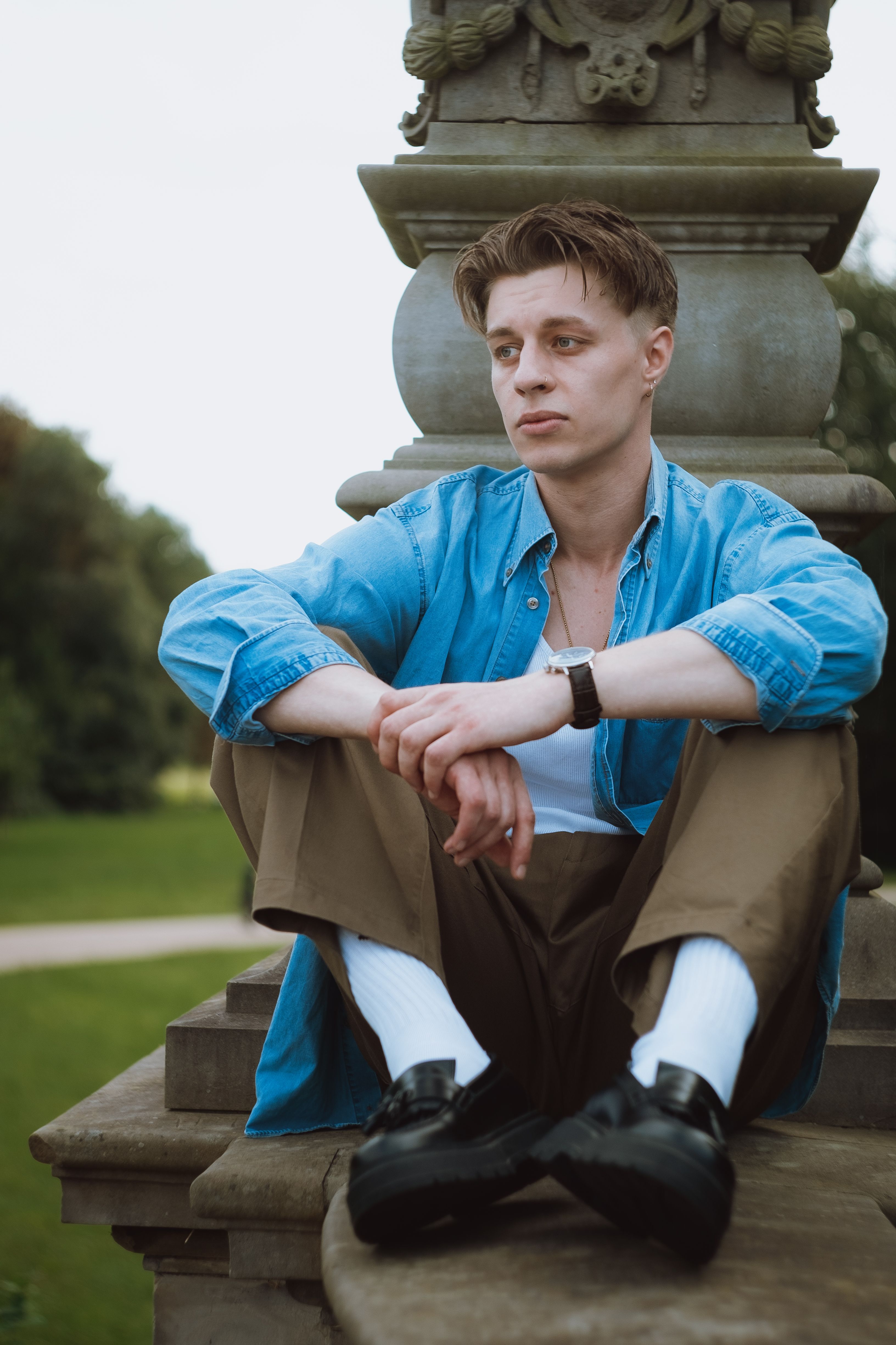 Casual portrait of a young man sitting on a stone monument in a park.