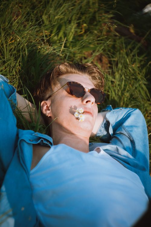 Free A man in sunglasses enjoys a sunny summer day lying on the grass with a flower on his face. Stock Photo