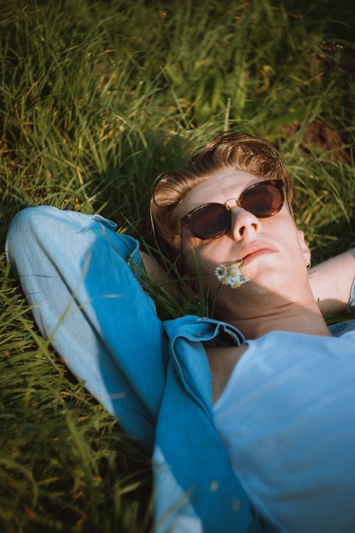 Free Young woman in sunglasses relaxing on grass in summer sun, enjoying leisure time outdoors. Stock Photo