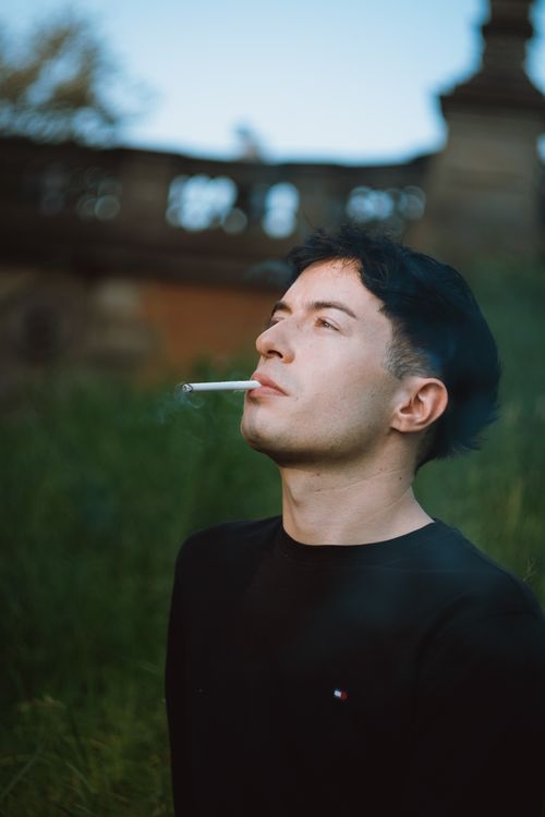 Free Portrait of a man smoking outdoors, exuding a vintage feel and thoughtful mood. Stock Photo