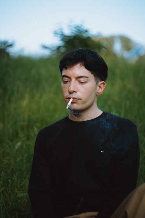 Free A man sits outdoors, smoking a cigarette surrounded by summer greenery. Stock Photo