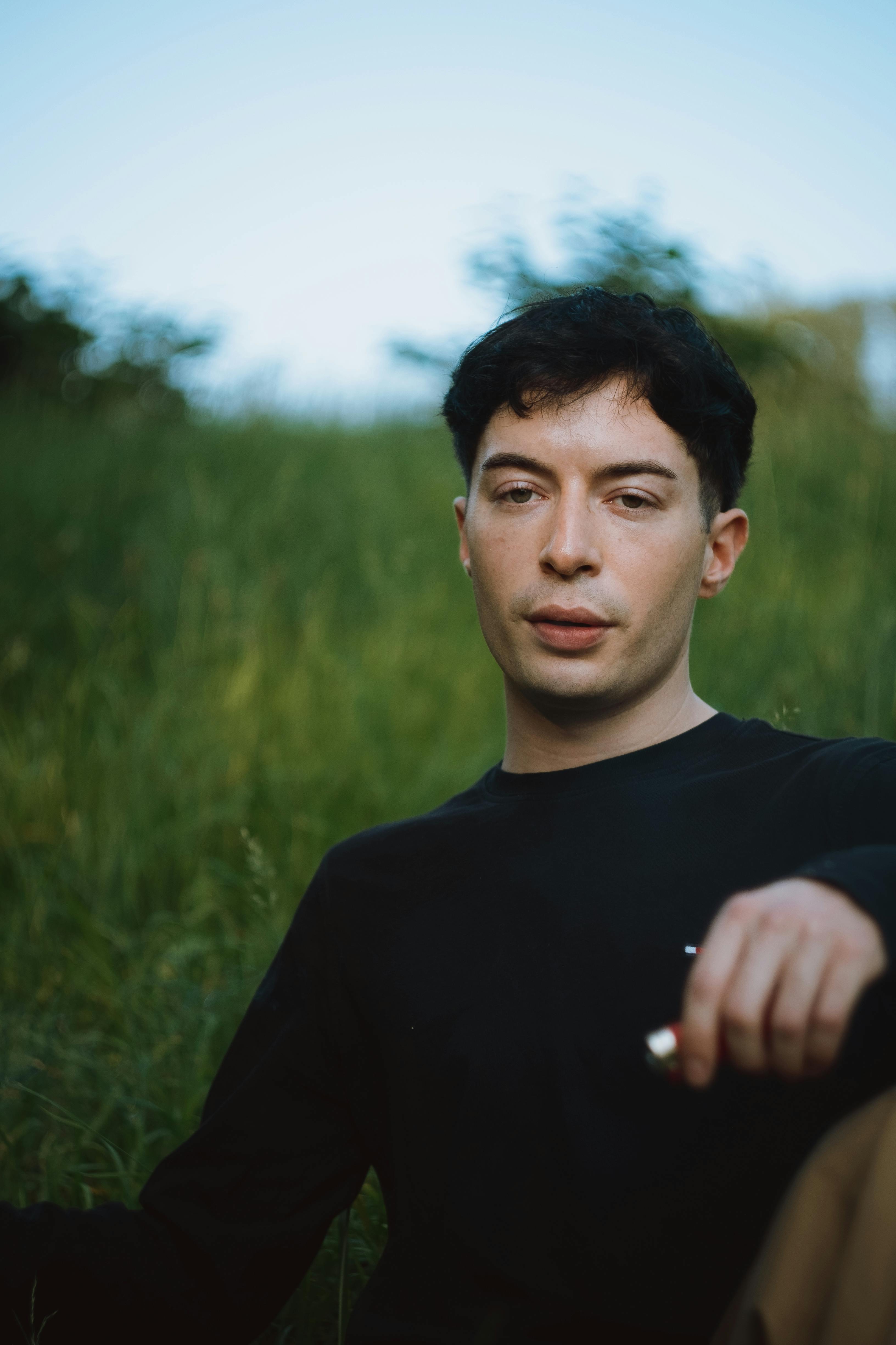 a man sitting in a field with his hand on his chin