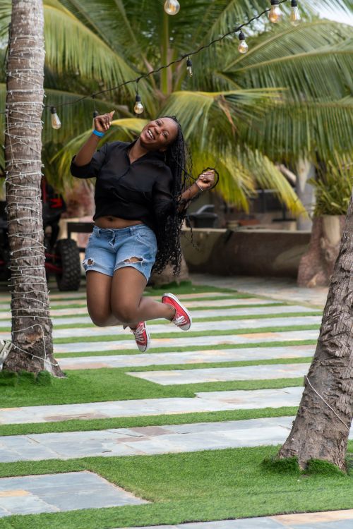 Free A woman joyfully jumps in the air outdoors amongst palm trees, expressing happiness and freedom. Stock Photo