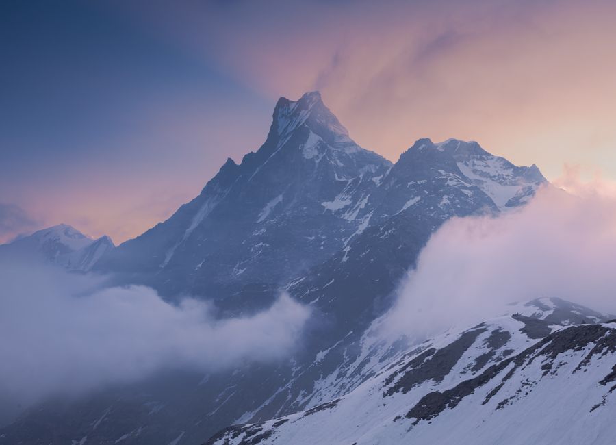 Stunning view of a snow-capped Himalayan mountain peak surrounded by clouds at sunset.