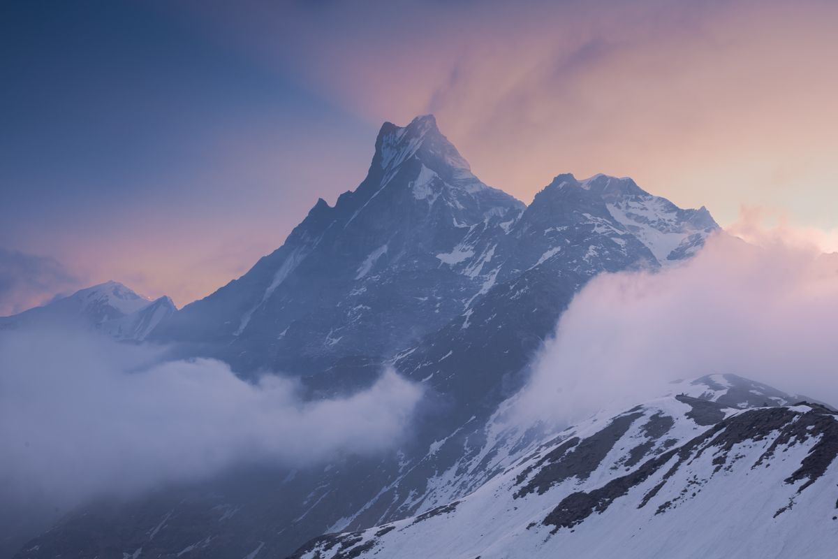 Lone trekker with backpack standing on dramatic Himalayan ridge looking out over sea of clouds and snow peaks