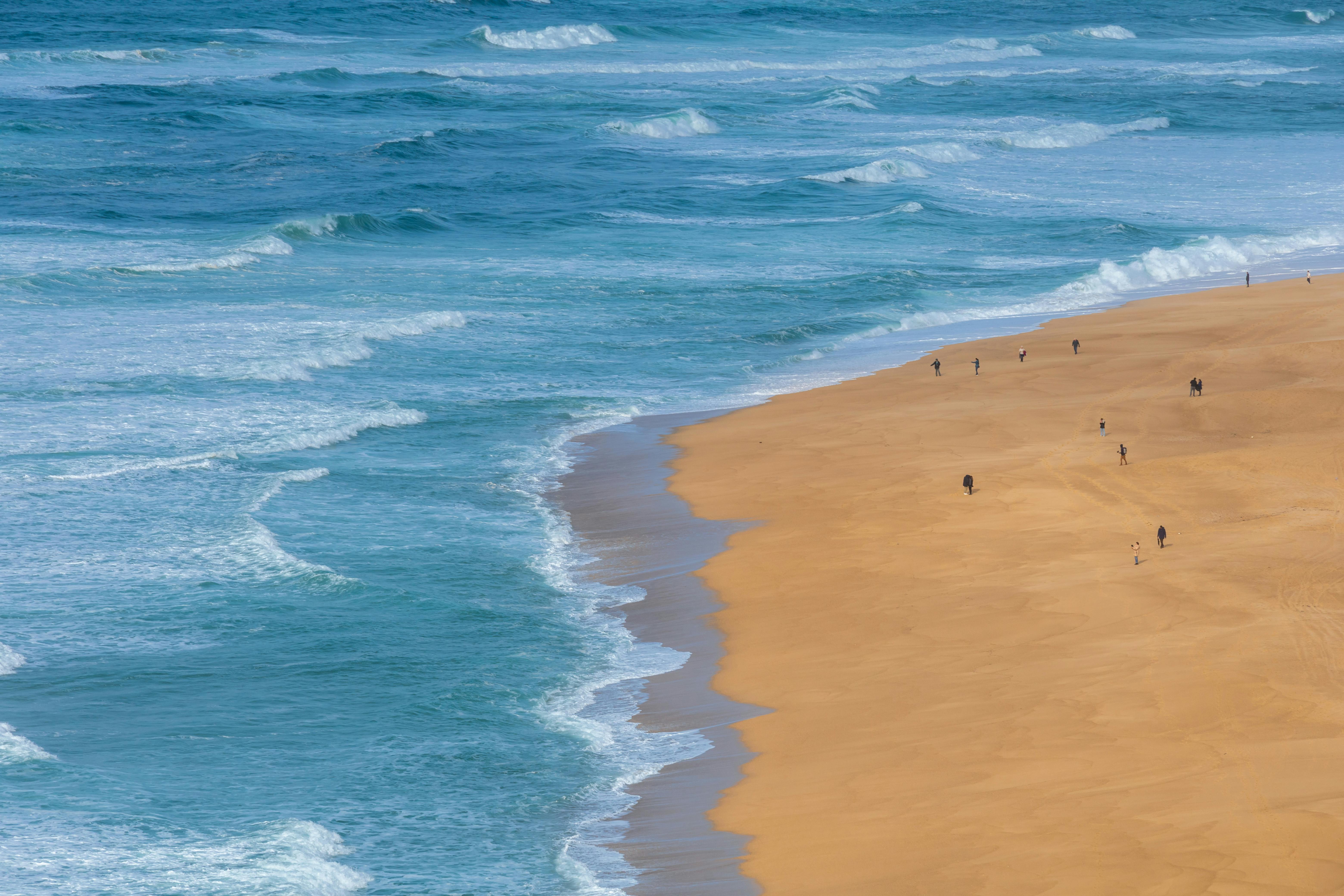 Stunning aerial capture of a sandy beach with waves and people walking along the shoreline.