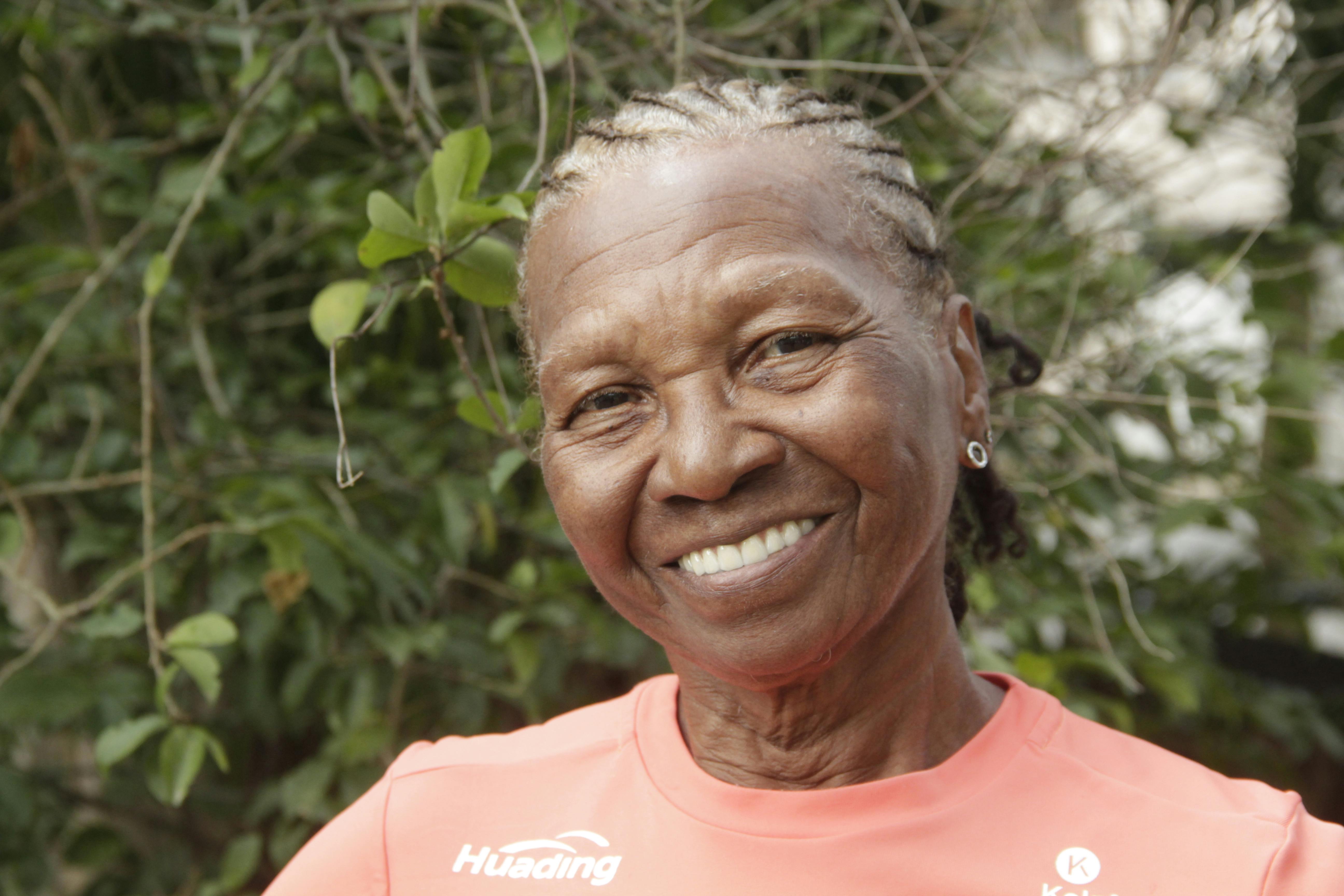 A cheerful elderly woman enjoying a sunlit outdoor setting, showcasing a warm smile.