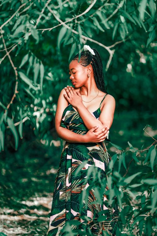 Free Woman in a tropical leaf pattern dress posing amidst lush green foliage. Stock Photo