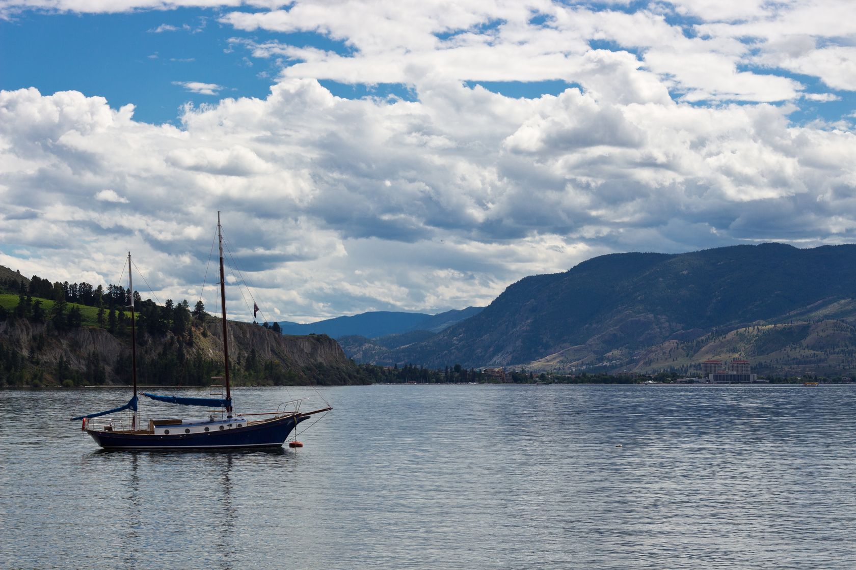 Peaceful scene with a boat on Okanagan Lake, surrounded by mountains and clouds in Kelowna, BC.