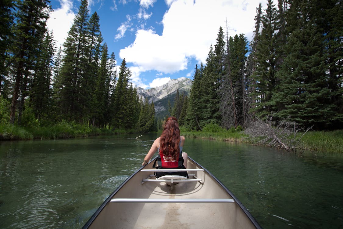 Woman Sitting On Canoe On River Near Trees