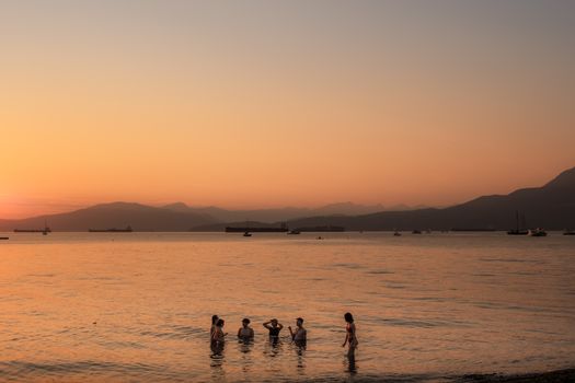 Silhouetted group of friends enjoying a sunset swim along the Vancouver shoreline.