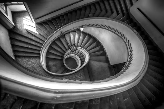 一张从上方拍摄的螺旋楼梯黑白照片，展现了建筑之美