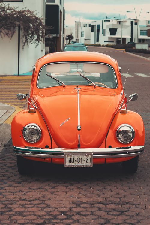 Free Vintage orange Volkswagen Beetle parked on a cobblestone street in Mexico, highlighting retro charm. Stock Photo