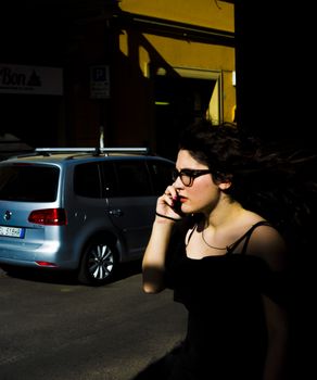 一名妇女一边打电话，一边走过城市街道，阴影被戏剧性地投射出来