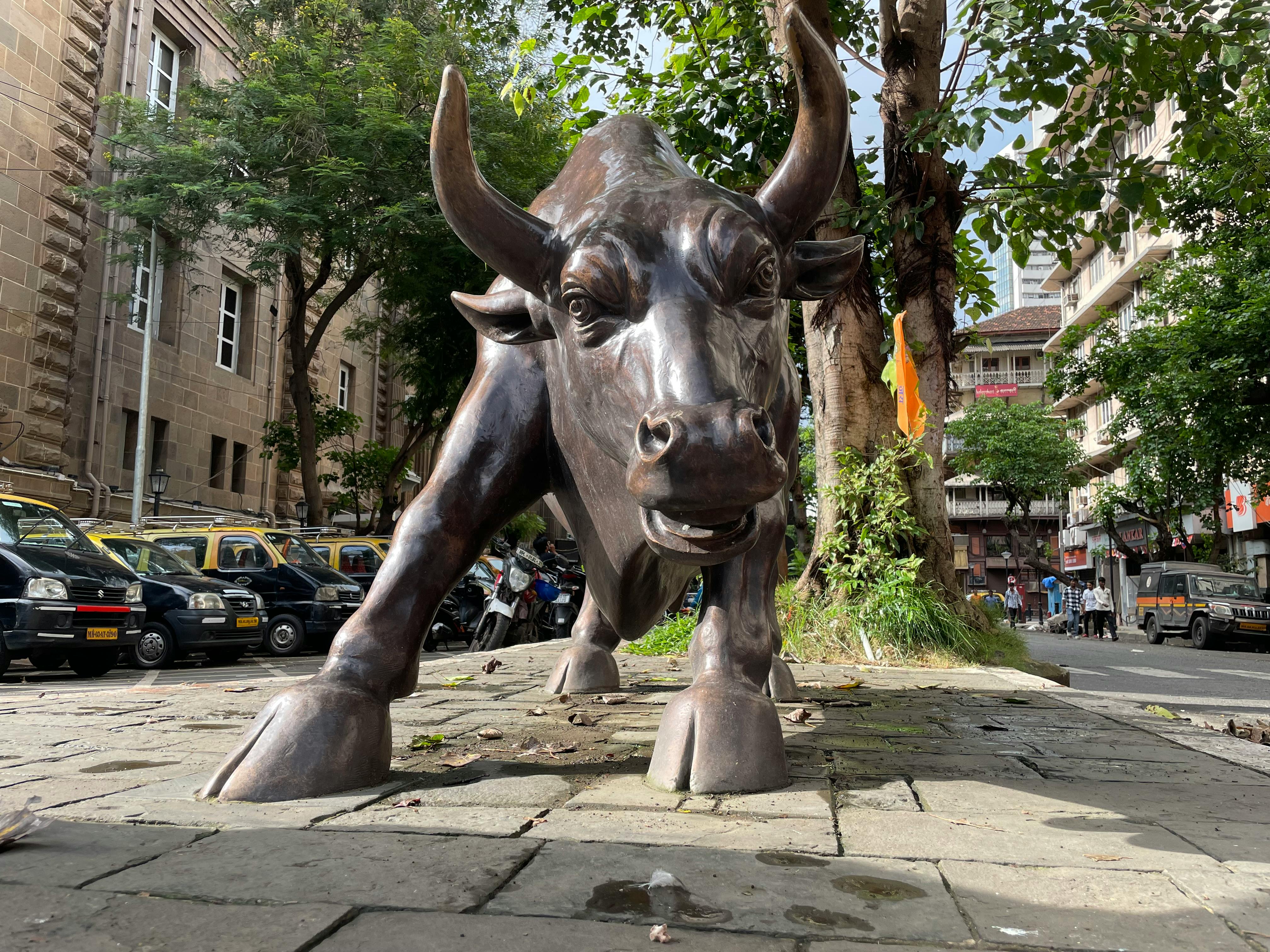 A prominent bull statue amidst a bustling urban street scene showcasing art and architecture.