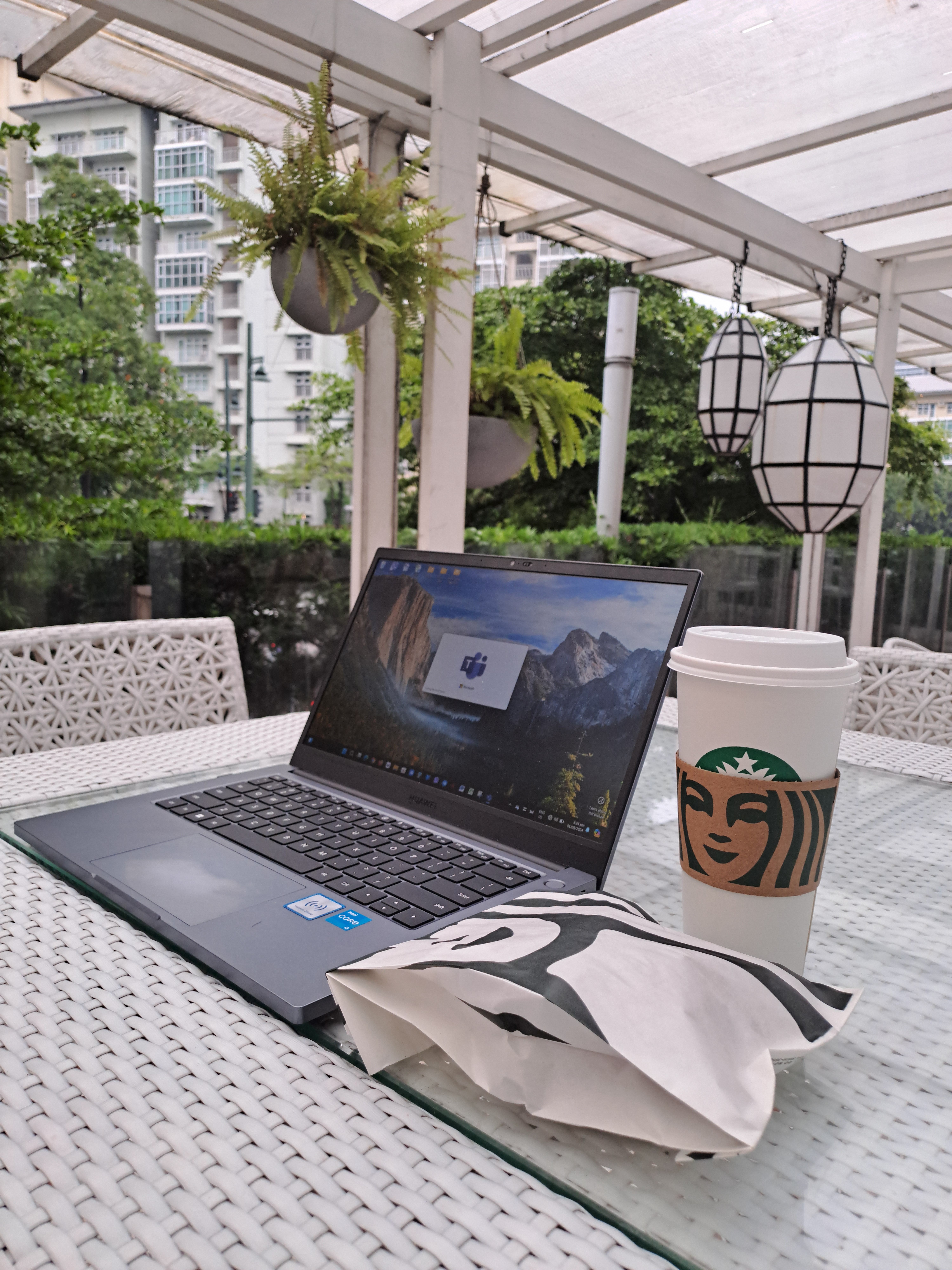 Cozy outdoor workspace with laptop, coffee, and snacks on a wicker table.