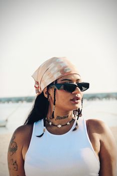 Stylish woman with bandana and sunglasses at a sunny beach, exuding summer fashion vibes.
