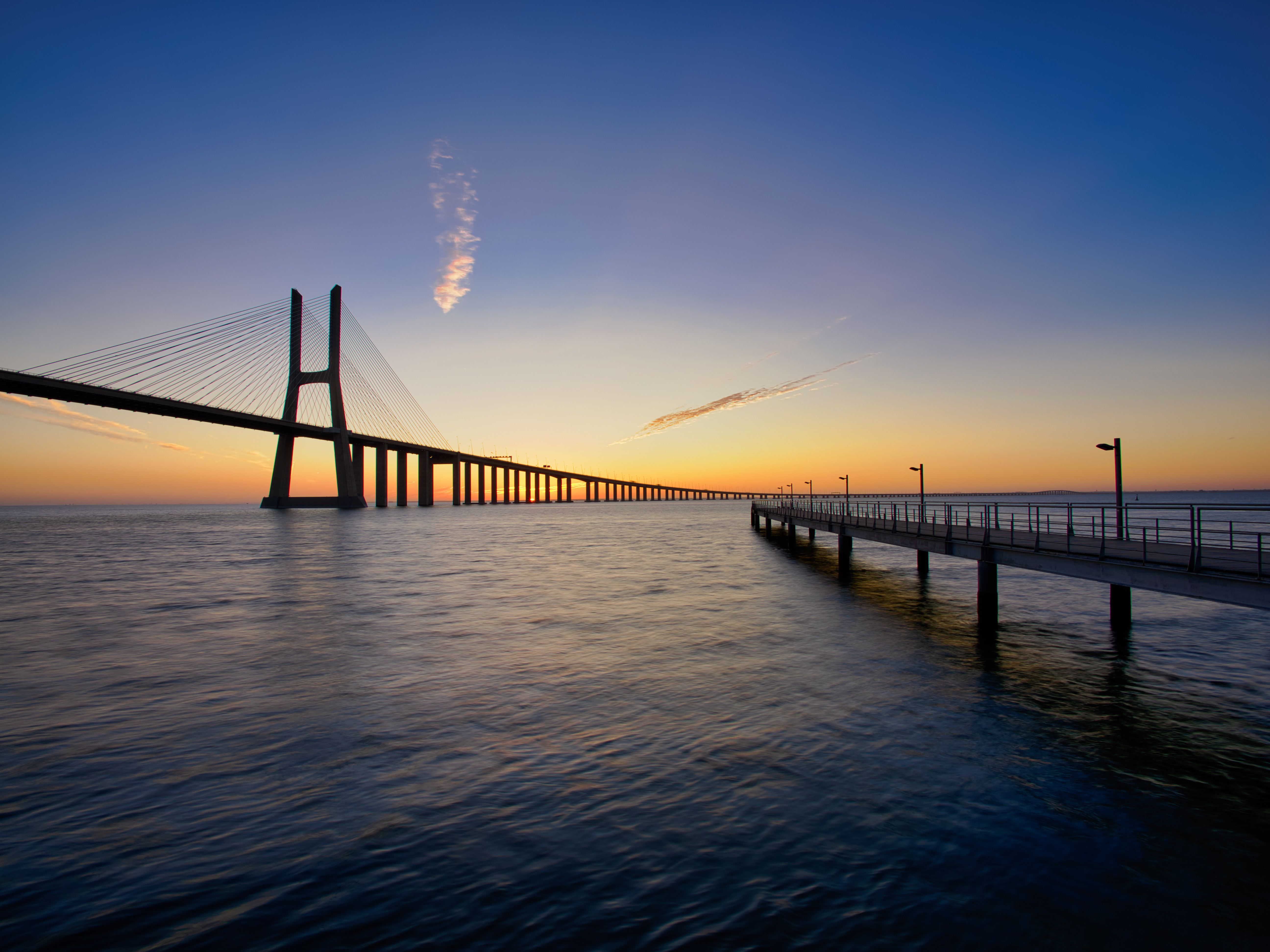 Tranquil sunset view of the Vasco da Gama Bridge stretching over calm ocean waters.