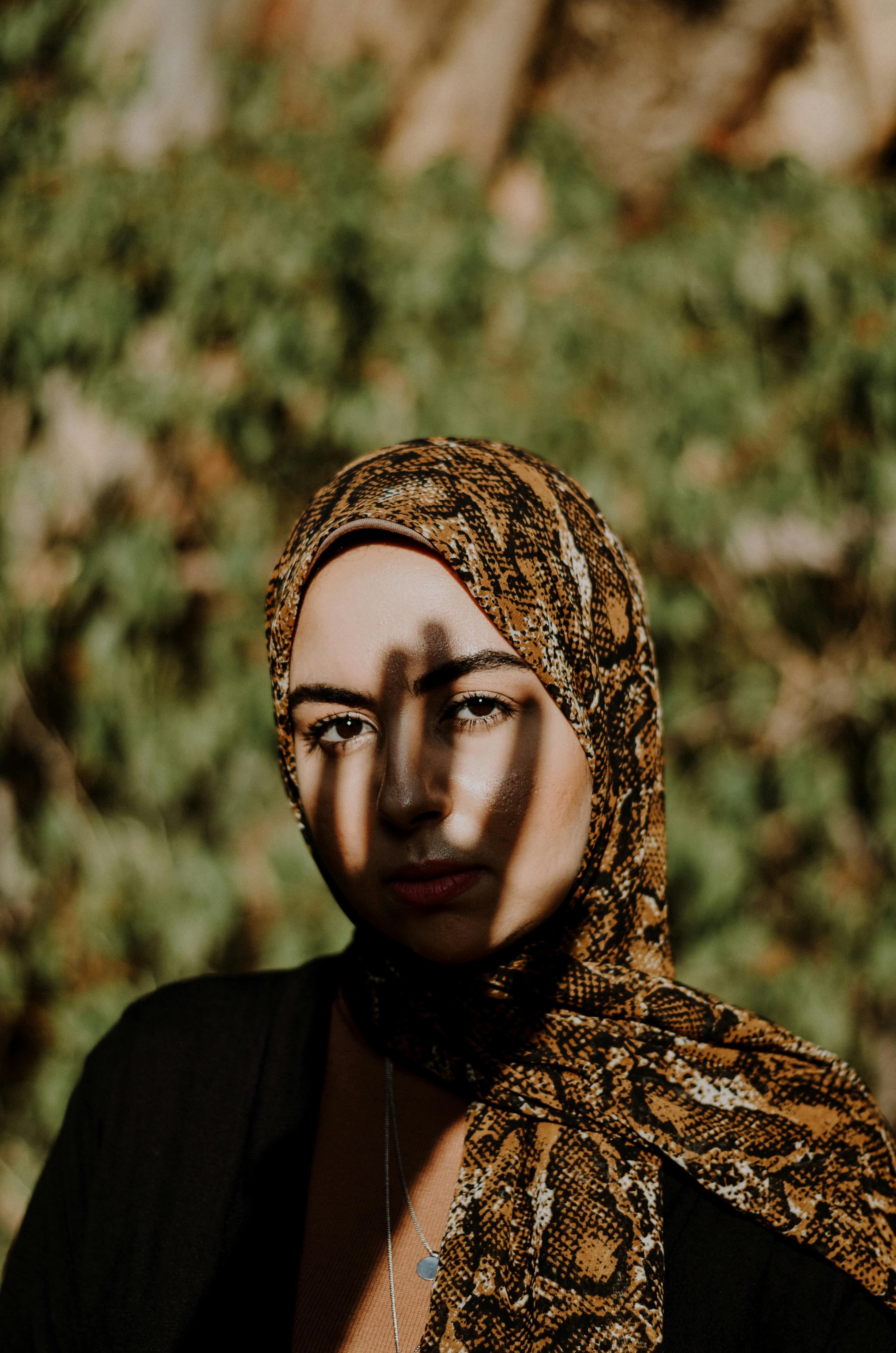 Artistic outdoor portrait of a woman in a patterned hijab with dramatic lighting and shadows.
