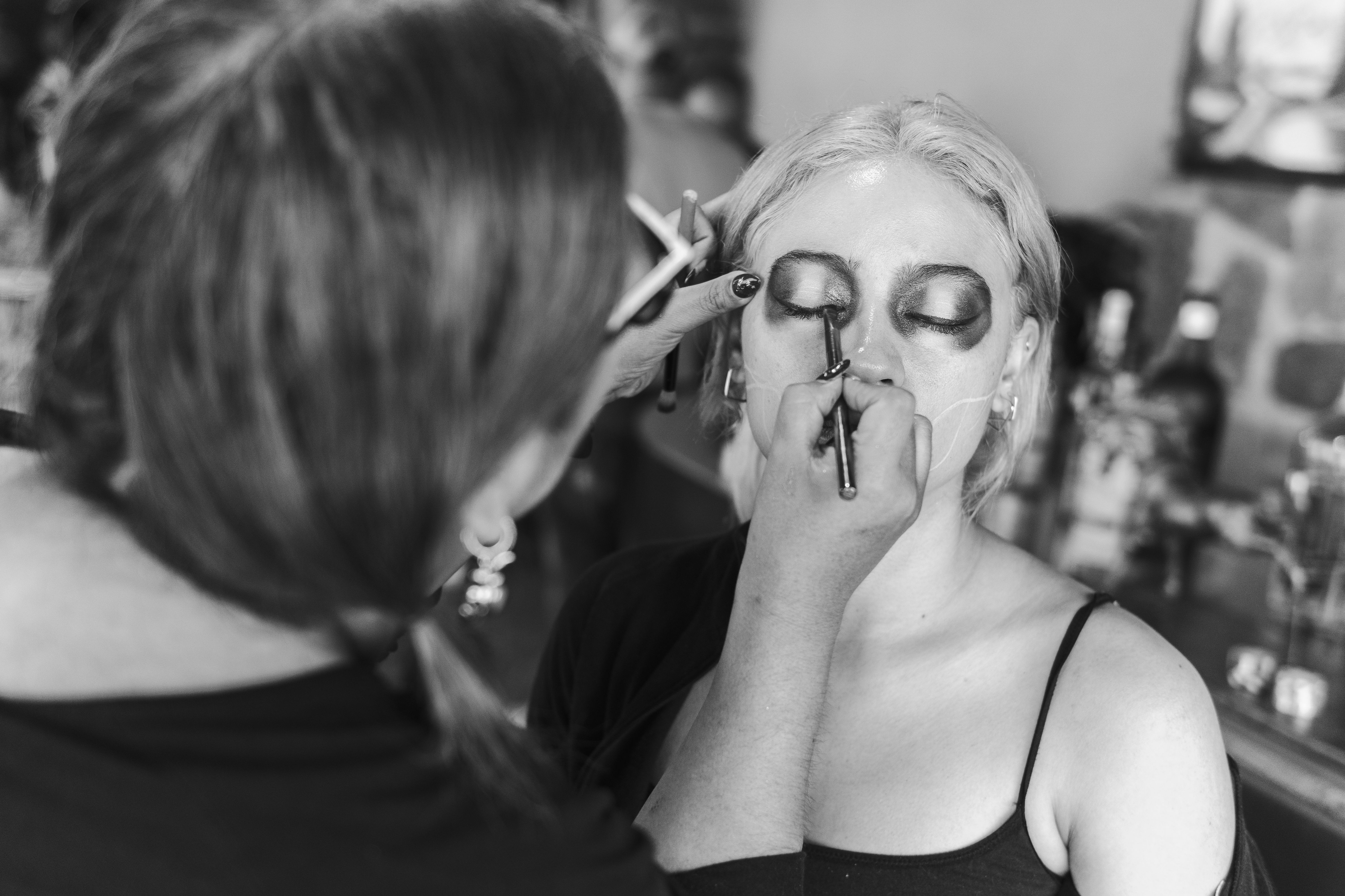 A woman having traditional Dia de los Muertos makeup applied in Mexico City, black and white photo.