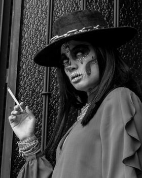 Black and white portrait of a woman with Catrina makeup holding a cigarette in Mexico City.