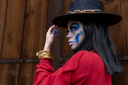 Free Side view of a woman with Day of the Dead makeup, wearing a hat and red dress, showcasing Mexican culture. Stock Photo