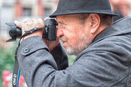 Free Elderly man in a hat taking photos with a camera outdoors. Street photography moment. Stock Photo