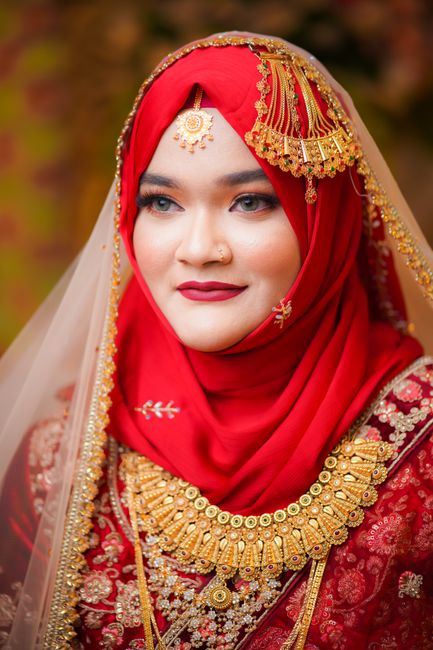 Bangladeshi bride in red wedding dress with intricate jewelry and makeup, showcasing cultural elegance.
