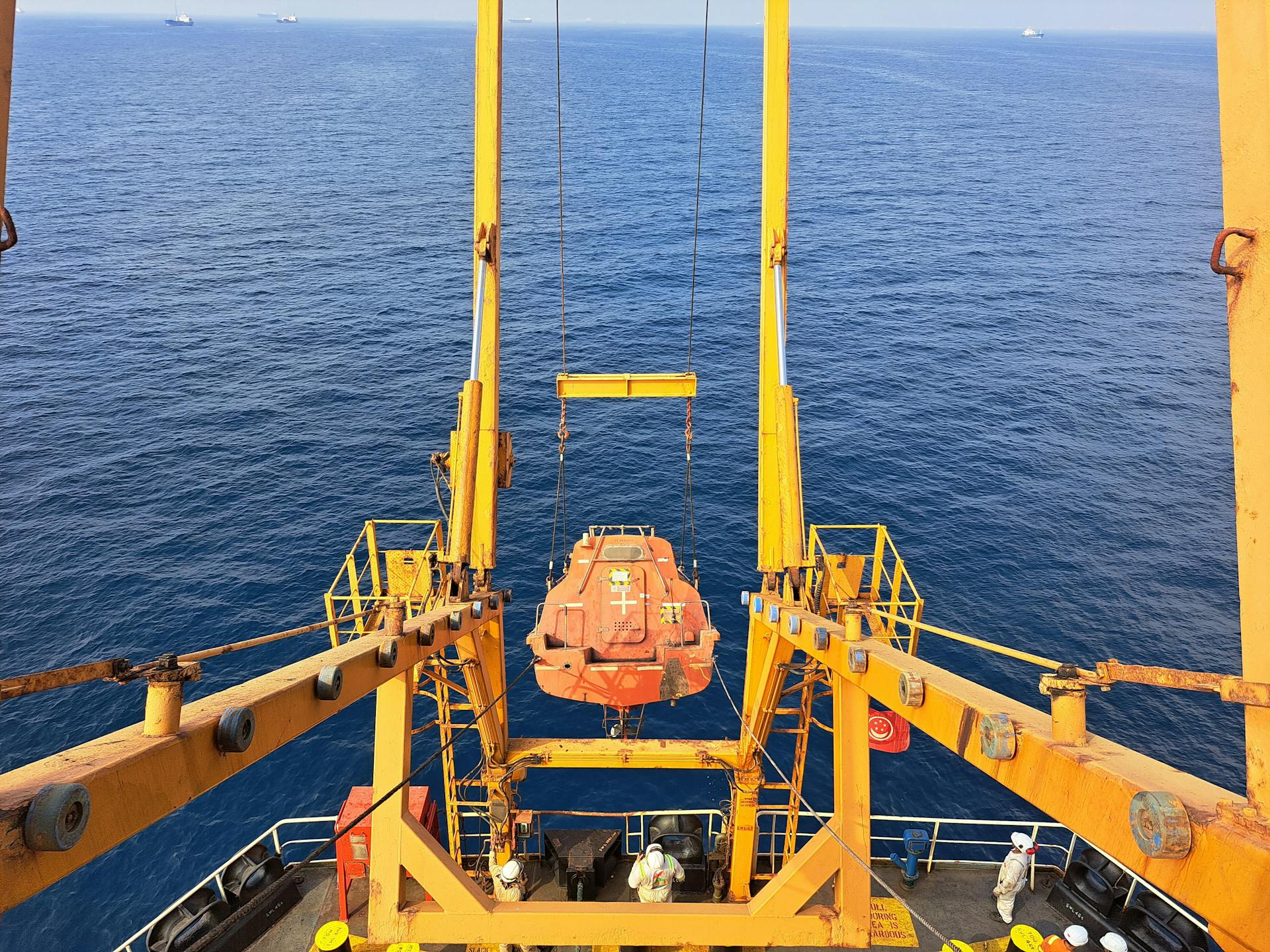 Lifeboat hanging over the ocean from a cargo ship, depicting maritime industry and safety.