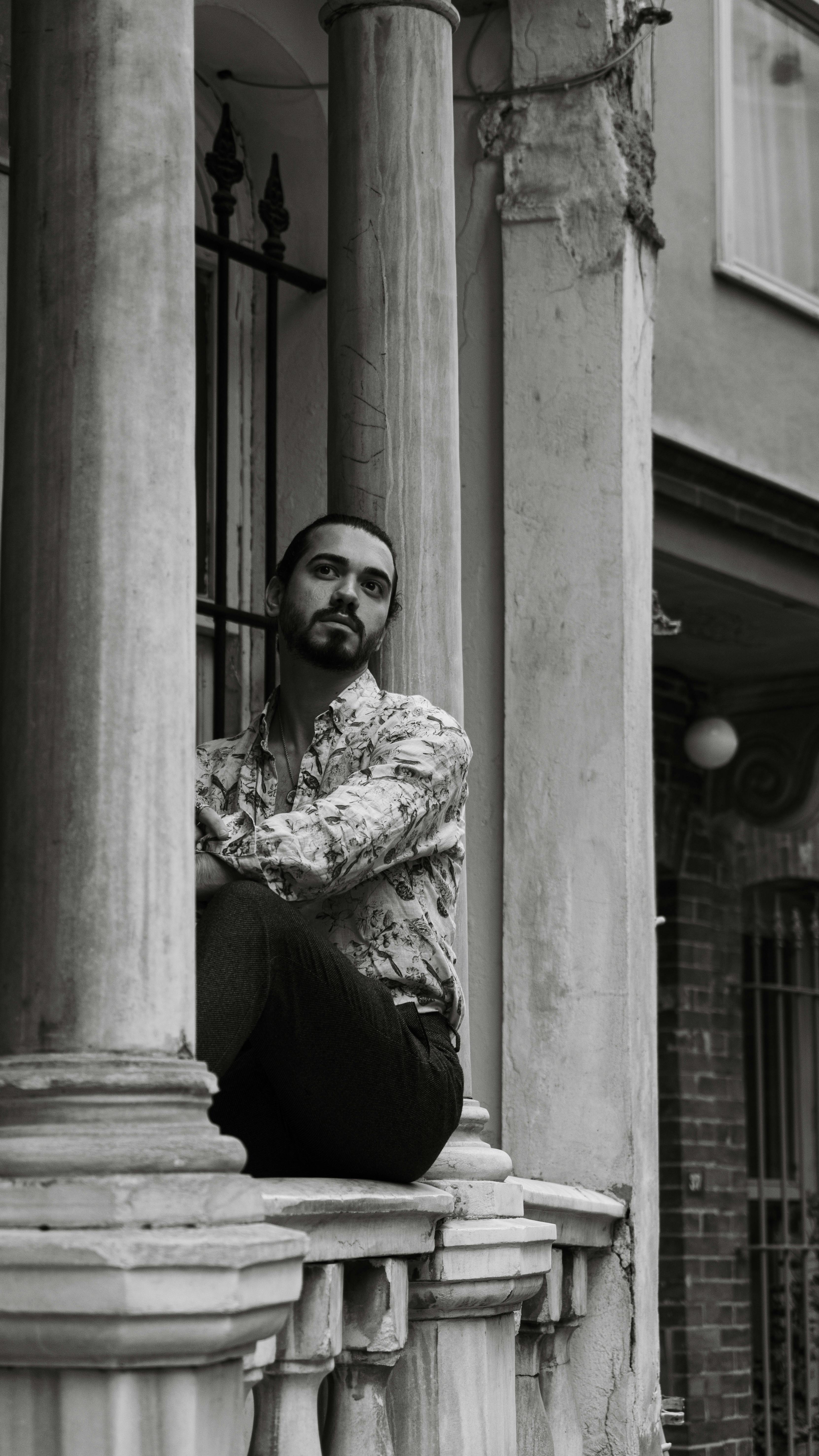 Black and white portrait of a man seated on a historic balcony with columns, exuding a reflective mood.