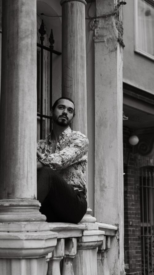 Free Black and white portrait of a man seated on a historic balcony with columns, exuding a reflective mood. Stock Photo