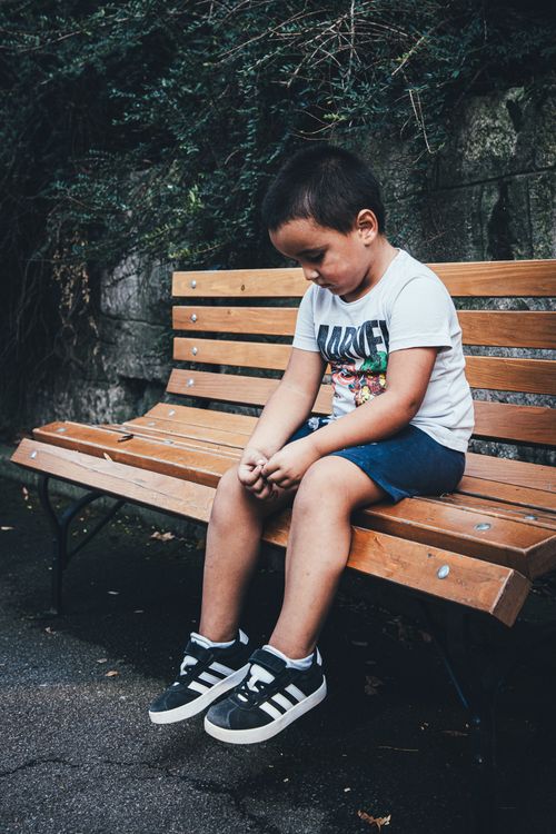 Free A young boy sits on a wooden bench outdoors, appearing thoughtful and contemplative. Stock Photo