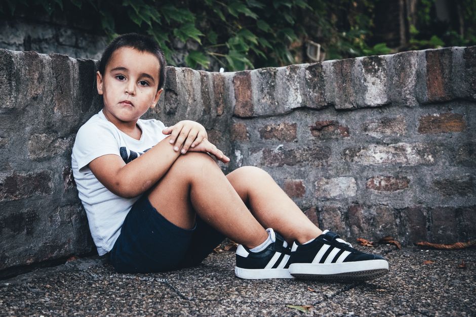 Retrato de un niño sentado junto a una muro de piedra, mostrando un estilo urbano casual.