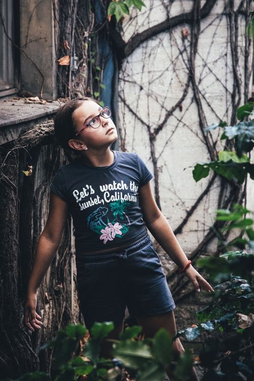 Free Child looking up in an urban garden with leafy vines and casual wear. Stock Photo