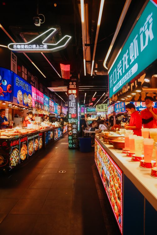 Free Explore the lively atmosphere of a neon-lit street food market with bustling vendors and glowing signage. Stock Photo