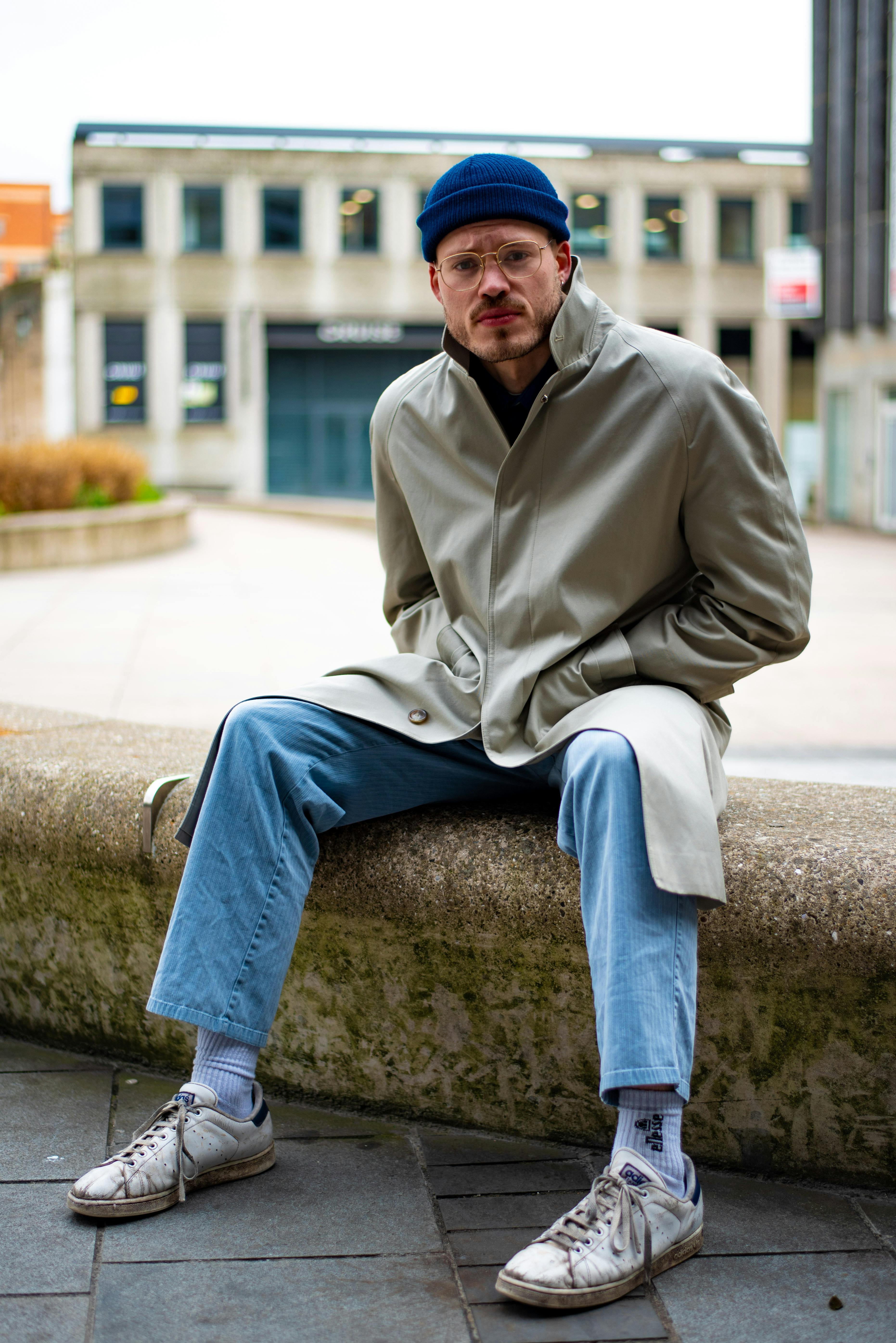 a man in a coat and jeans sitting on a stone wall