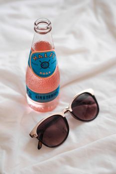 Refreshing pink gin tonic paired with stylish sunglasses on a white background.