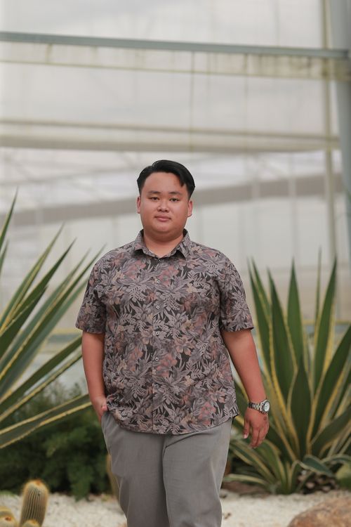 Free Portrait of a young man standing in a garden, wearing a casual shirt and enjoying a sunny day. Stock Photo