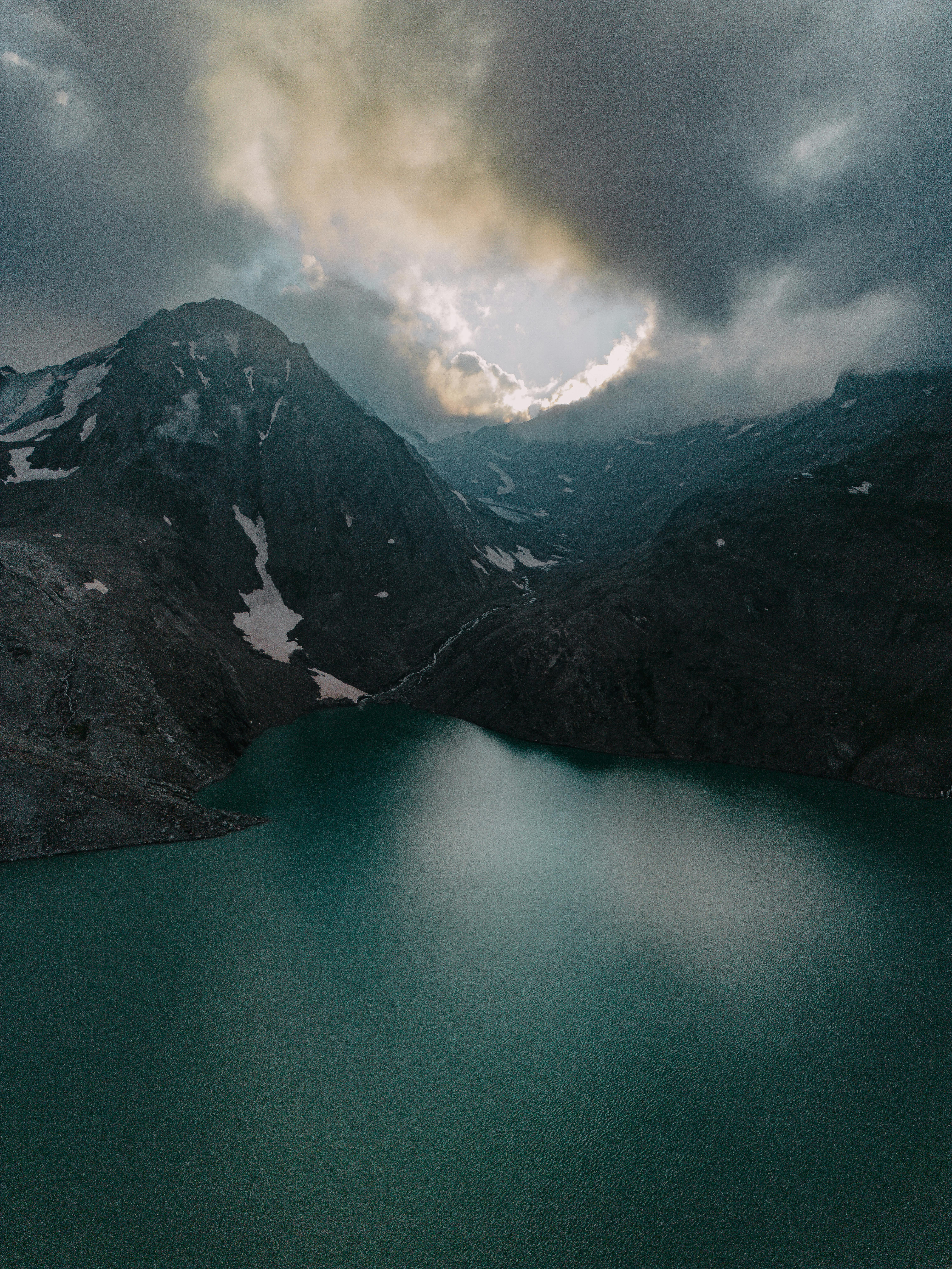 A serene mountain lake set against a backdrop of stormy clouds and rugged peaks, showcasing nature's raw beauty.