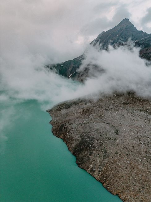 Drone view of a serene mountain lake surrounded by mist and rugged peaks.