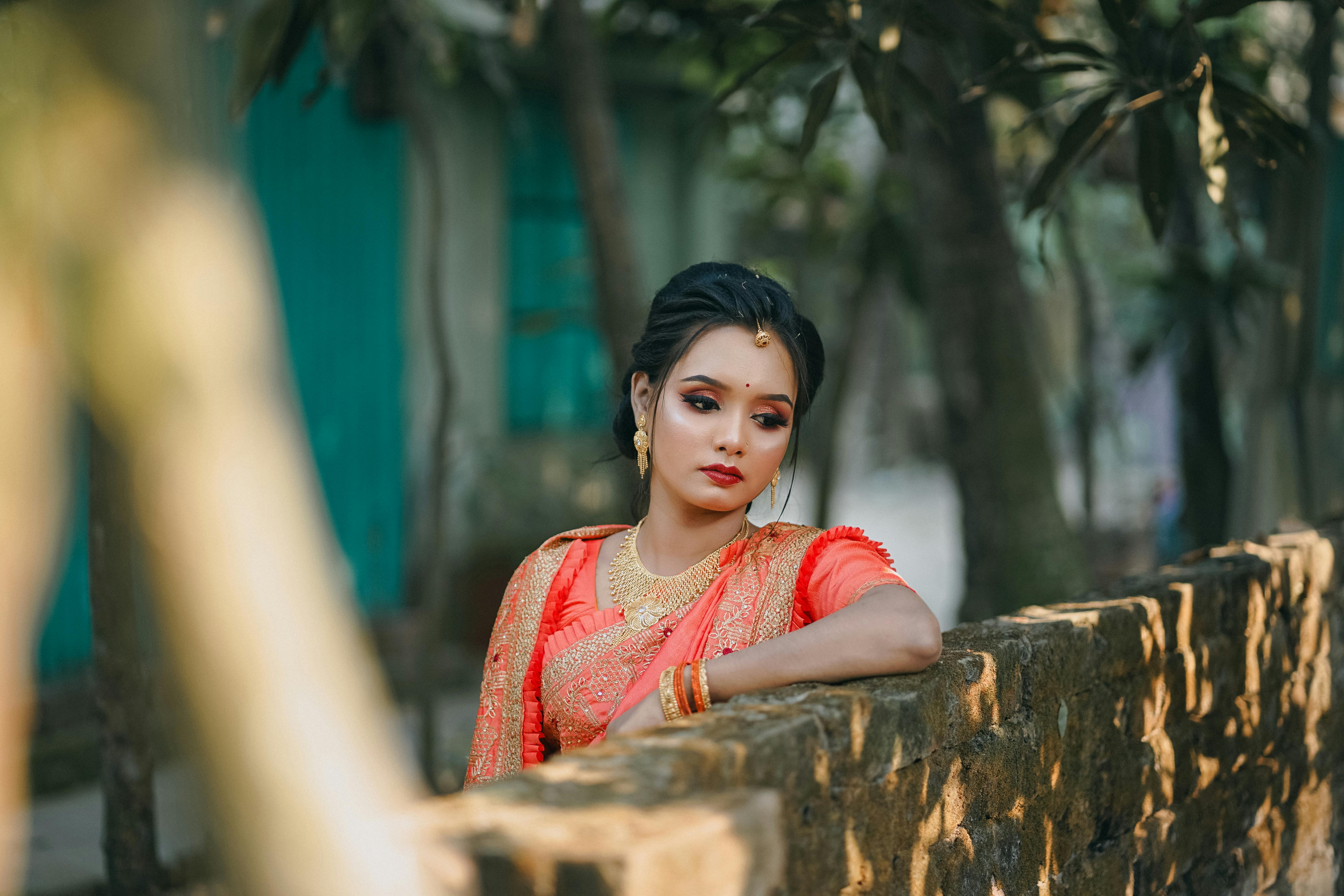 a beautiful woman in an orange sari leaning against a wall