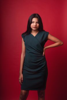 A young woman posing elegantly in a green dress against a red background.