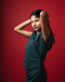 Portrait of a young South Asian woman posing elegantly in a studio with a red background.
