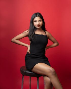 Studio portrait of a young woman in a black dress against a red backdrop.