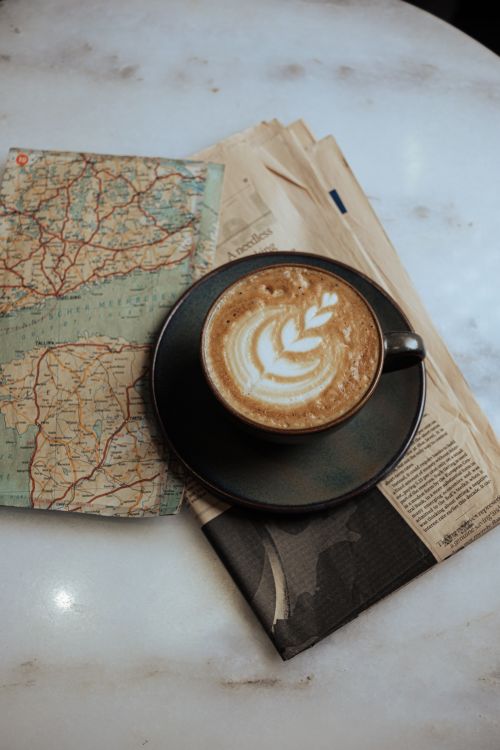 Free Flat lay of cappuccino with latte art on a table with a map and newspaper. Ideal for travel and lifestyle themes. Stock Photo